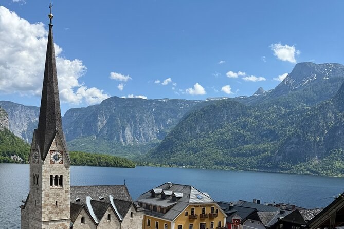 A slender church spire above the rooftops, the lake and the mountains behind