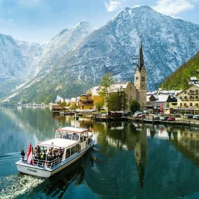 A lake boat passing the village under snow-dusted mountains