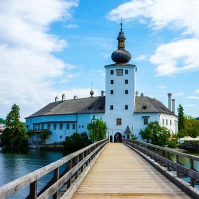 A white lake palace with an onion-domed tower at the end of a wooden bridge