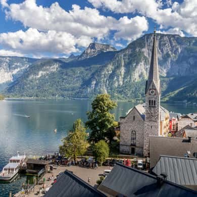A church spire in front of grey peaks and the lake